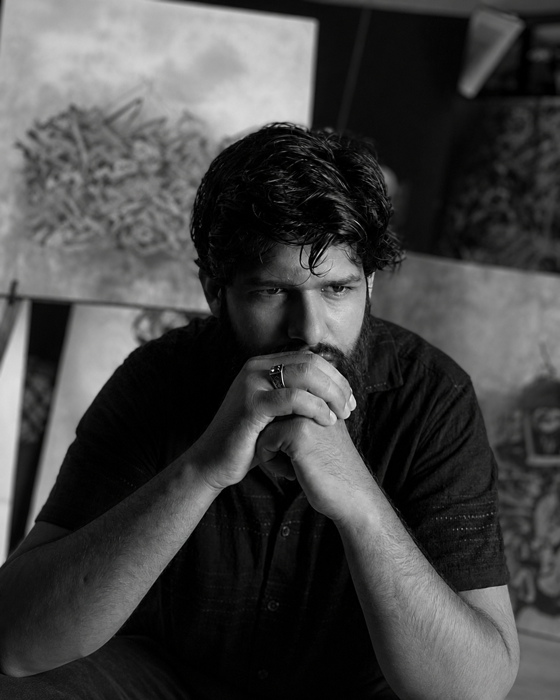 Khuzaima Ayaz seated in his studio with artworks behind him